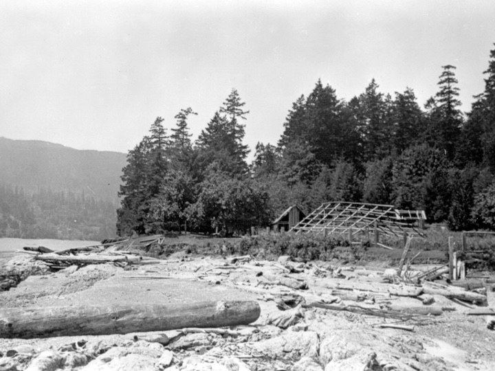 Hwu’ne’nuts in the late 20’s early 30’s, showing the ruins of Charlie Joseph’s gable roofed house with the longhouse in the foreground.. Salt Spring Island Archives.